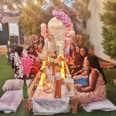 Here is a candid moment from a beautiful garden bridal shower. The low picnic table, illuminated by candles and lanterns, creates a warm and intimate atmosphere for the bride-to-be and her friends.