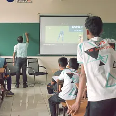 A teacher uses a cricket match video projected in the classroom to explain rules and tactics, blending sports analysis with academic learning.