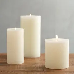 A collection of lit ivory pillar candles on a wooden surface, demonstrating their warm and gentle light. These are perfect for creating a serene and calming environment in spas or for candlelight dinners.