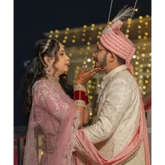 A tender moment captured under the soft glow of string lights. The bride, in her beautiful pink lehenga, shares a loving glance with her partner, creating a classic and elegant nighttime portrait.