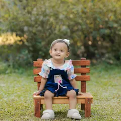 A simple prop like this small wooden bench is perfect for an outdoor baby portrait. It helps position the child comfortably while blending in with the natural park surroundings.