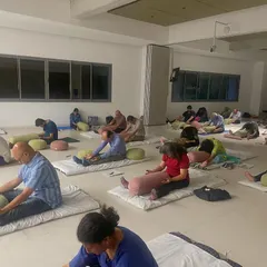 A moment from a community workshop where participants engage in gentle forward folds using bolsters for support. These mindful movements help release physical tension before we move into deep relaxation.
