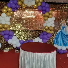 I can bring any birthday theme to life. This Disney princess theme features a circular balloon arch in purple, gold, and white against a sparkling sequin backdrop, complete with character cutouts of Jasmine and Elsa for a magical celebration.