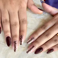 This elegant manicure features a deep burgundy polish paired with accent nails showing intricate, hand-painted leaf patterns on a sheer nude base.