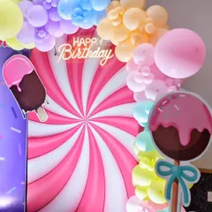 A detail shot of the candy-themed backdrop, featuring a giant swirling lollipop design and a neon 'Happy Birthday' sign.
