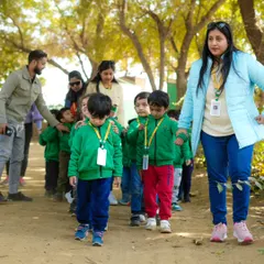 A teacher guiding a line of young students on a walk through the farm.