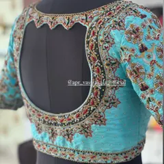 A heavily embroidered blouse in a striking sky blue, shown on a mannequin to highlight the dramatic back cutout. The entire surface is covered in floral zardosi work.