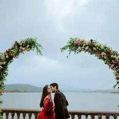 A romantic kiss under a heart-shaped floral arch, set against a serene lake. This is a perfect example of a planned, yet emotionally resonant pre-wedding photograph.