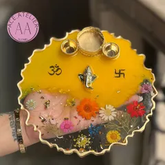 This pooja thali features a bright yellow top, symbolizing happiness and auspiciousness. The clear bottom half is filled with colorful preserved flowers and gold flakes.