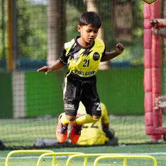 A young player shows great form and concentration while jumping over agility hurdles. These drills are essential for improving coordination, speed, and balance on the field.
