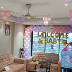 A full room decoration to welcome a new baby home. This setup includes a large balloon arch over the window with "Welcome Baby" foil letters, along with balloon bunches on the ceiling and a cute unicorn playhouse prop.