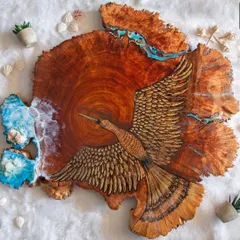 A unique piece combining wood burning art with resin. This large wood slice features a hand-sketched bird with detailed feathers, set against a backdrop of blue resin ocean waves.
