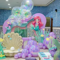 A beautiful mermaid-themed setup for Noura's 6th birthday. It features iridescent bubble balloons, a giant clamshell for photos, and cutouts of Ariel and other sea life.