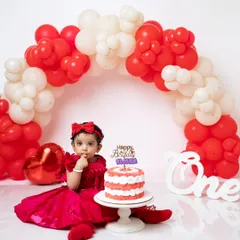 A full view of the red and white cake smash setup, complete with a balloon arch and a "One" sign to mark the special milestone.