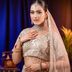 A graceful and polished look featuring a model in a shimmering silver-white lehenga. The soft studio lighting highlights the subtle glow of the makeup and the intricate details of the diamond necklace and traditional bangles, creating a perfect sangeet or reception look.