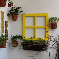 Get creative with your wall garden! Here, we used a bright yellow window frame as a centerpiece, surrounded by terracotta face planters and other decor to create a fun and eclectic balcony wall.