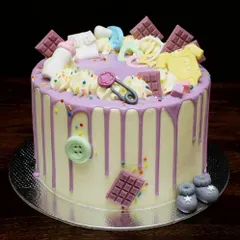 An adorable "Oh Baby!" shower cake. This design has a purple drip and is loaded with cute, handmade fondant baby items like booties, a bottle, a onesie, and a pacifier, all in a pastel color palette.