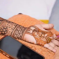 A candid shot of me personalizing a bride's mehendi with a dulha-dulhan figure, with her phone nearby for design reference.