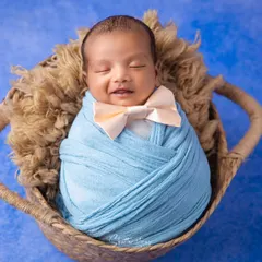 A smile in his sleep. This little gentleman is dressed in a blue swaddle with a tiny bow tie, looking absolutely adorable and content in his basket.