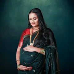 A beautiful portrait of a mom-to-be in a traditional dark green saree with a red border, complete with a classic nose ring and gold jewelry.