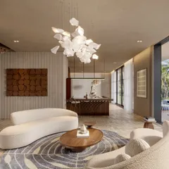 This perspective of the Siroi Lilly living room highlights the open, airy feel. The design connects the seating area to a bar and dining space in the background, all unified by a consistent material palette and a stunning feature chandelier.