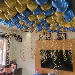 A room ceiling covered in blue and gold helium balloons with dangling ribbons for a festive party atmosphere.