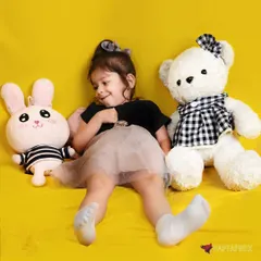 A candid and adorable moment captured in the studio. The young girl is surrounded by stuffed toys, creating a sweet and playful scene that feels natural and full of personality.