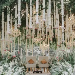 An intimate and elegant mandap setup nestled in a natural, green environment. We used cascading strings of tuberose and blush pink florals to create a delicate curtain, perfectly framing the couple's seating.