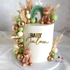 A rustic and trendy baby shower cake in shades of green and gold. This design features a teddy bear theme, a muted green rainbow, and dried pampas grass.