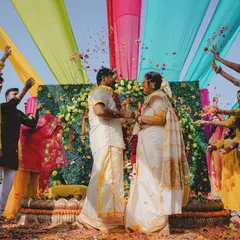 A beautiful moment from a South Indian wedding ceremony, with family showering the couple with flowers under a colorful canopy.