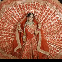 A full view of a traditional red bridal lehenga, showing the detailed embroidery on the double dupatta and the rich texture of the fabric.