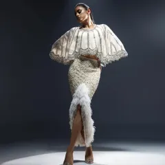 An ivory ensemble featuring a cape-style top and a fitted skirt with feather details. This look is the definition of modern couture, ideal for a bride who wants a fashion-forward look for her reception.