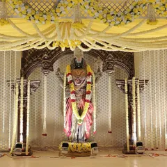 This angle highlights the intricate ceiling of the mandap, covered in yellow fabric and a web of fresh flower garlands. The stage is lit with spotlights to focus on the ceremony area.