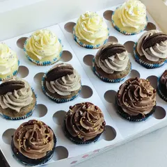 A slightly different view of the 12-piece classic assortment box, showing the rich swirls of buttercream and the simple, elegant toppings like sprinkles and a mini Oreo.