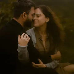 A close, intimate portrait of a couple in a lush, green setting. The soft, natural light and their gentle embrace create a feeling of warmth, peace, and deep connection.