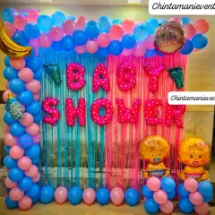This is a classic baby shower decoration with a pink and blue theme, perfect for when the gender is a surprise. The backdrop includes a tinsel curtain, 'Baby Shower' foil letters, and cute baby-themed foil balloons.