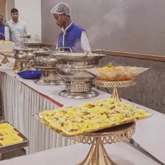 A staff member serving guests at a buffet. The setup includes elegant tiered serving platters for appetizers and silver chafing dishes for main courses.