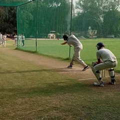 A batsman plays a powerful shot during net practice, with the wicketkeeper ready behind the stumps. This simulates match conditions to improve timing and shot selection.