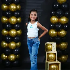 A confident young girl poses during her birthday shoot in our studio. The black and gold balloon decor adds a touch of glamour to the celebration.