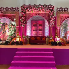 A stage fit for a queen's Mayra ceremony. The design is dominated by a rich magenta, with intricately carved arches, traditional artwork, and lush floral arrangements creating a truly royal ambiance.
