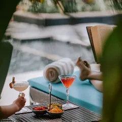 Two women relax by the pool with books and cocktails. This image captures the essence of a tranquil retreat, a perfect way to celebrate oneself or enjoy a getaway with a friend.