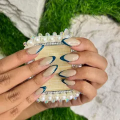 A modern twist on a classic, this reverse French manicure uses a neutral base on almond-shaped nails. A deep teal polish is applied along the cuticle line for a unique and stylish look.