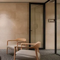 A quiet seating nook within the Elevate Clubhouse. The use of natural stone walls, terrazzo flooring, and minimalist wooden chairs creates a serene corner for relaxation or informal conversation.
