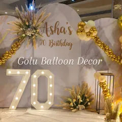 The main photo wall for a 70th birthday celebration. The setup includes the "Asha's 70 Birthday" custom text, marquee numbers, and floral accents with pampas grass.