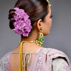 A classic for a reason. This elegant twisted bun, adorned with a cascade of fresh purple chrysanthemums, is a timeless choice for the main wedding day. It’s structured to hold the dupatta securely and stay perfect through all the ceremonies.