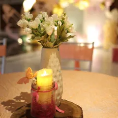 A detail shot of the table centerpiece from a butterfly-themed party. A simple white floral arrangement sits next to a candle in a jar, decorated with a small butterfly accent, creating a warm and enchanting ambiance.