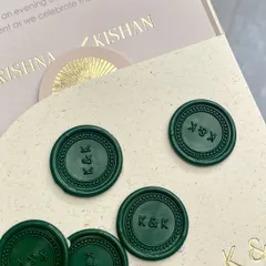 A close-up of custom wax seals in a deep emerald green, stamped with the couple's 'K&K' monogram. The seals are placed next to the gold-foiled invitation, showing how different textures can work together.