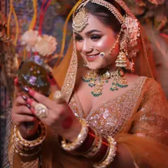 A candid moment as the bride looks into a mirror, her smile reflecting her joy. This is a classic Karwa Chauth themed shot.