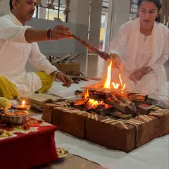 Two participants make offerings to the fire during a Ganapati Homam. This act of offering is a key part of karma yoga, performed with devotion and without expectation of personal gain.