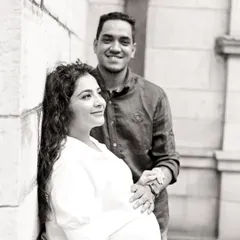 A beautiful black and white couple portrait against a simple architectural background. The image has a classic, elegant feel, focusing on their hopeful expressions and gentle interaction.